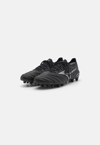 Black soccer cleats made of leather with a textured upper, featuring a white stripe accent and molded studs for traction on grass.