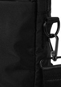 Schwarze Textiltasche mit strukturierter Oberfläche, einem robusten Reißverschluss und Metallbeschlägen, einschließlich eines Karabinerclips und Gurtbefestigungen.