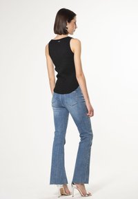 Top nero senza maniche con una finitura testurizzata; abbinato a jeans in denim azzurro chiaro a palazzo e scarpe argentate con tacco alto.
