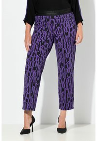 Fioletowe spodnie dresowe z nadrukiem w powtarzający się wzór "MODERN", z elastycznym pasem i skróconą długością. Materiał wydaje się lekki i elastyczny.