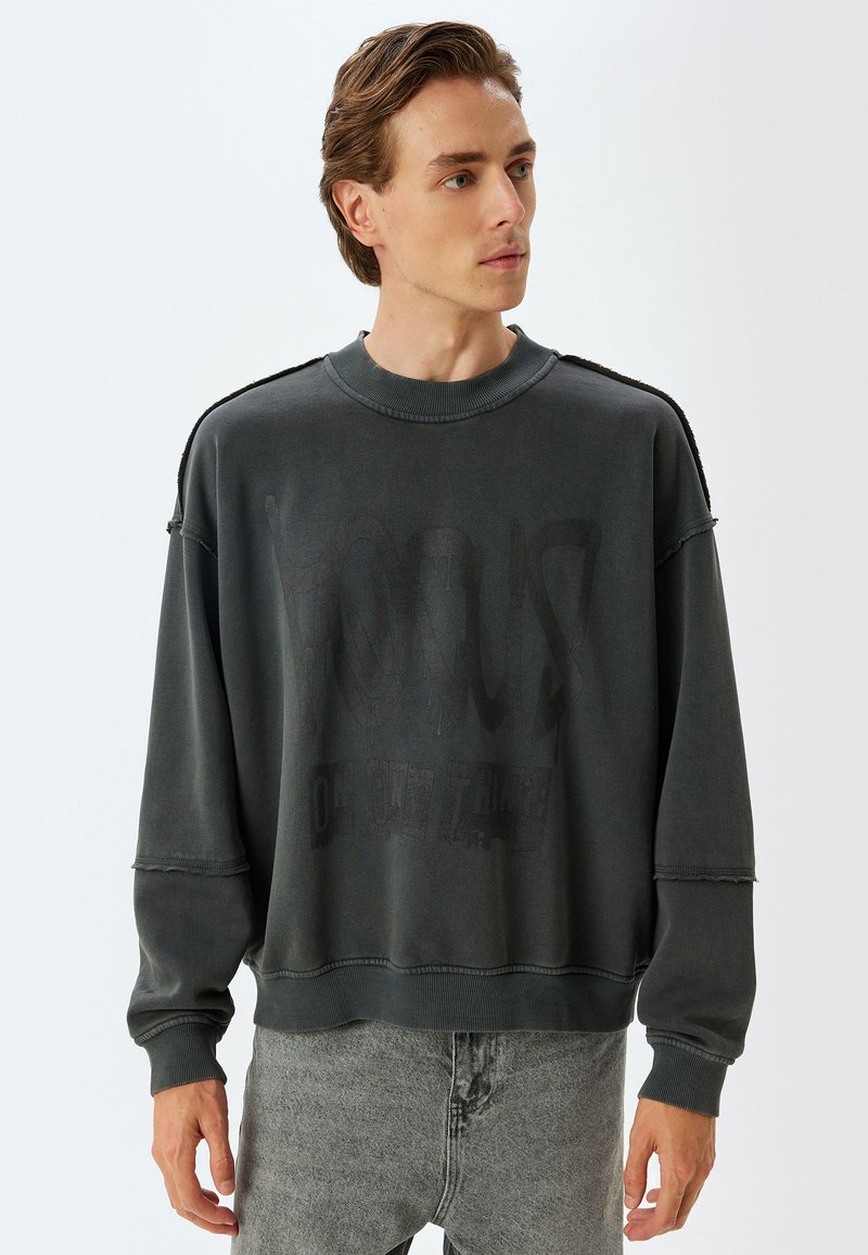 Donkergrijze oversized sweatshirt met een ronde hals, versleten randen en een vervaagde grafische print op de voorkant. Zachte, textuurstof met verlaagde schouders.