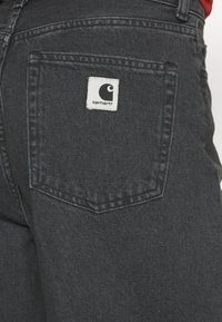 Black denim jeans featuring a back pocket with a white Carhartt logo patch, structured shape, and reinforced stitching detail.
