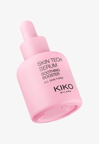 Botella gotero de vidrio rosa etiquetada como "Skin Tech Serum Soothing Booster", con un cuerpo redondeado y una tapa de gotero en forma de bulbo.
