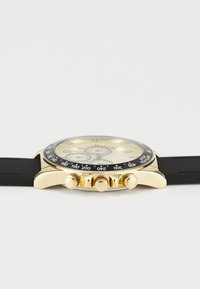 Montre dorée avec une lunette noire, un bracelet en caoutchouc et un cadran texturé présentant trois sous-cadrans et des marqueurs d'heure saillants.