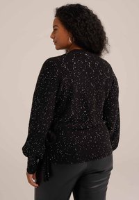 Črna pletena jakna z belimi spekli, z oprijetim pasom in napihnjenimi rokavi, teksturiranega materiala in zaobljenim hrbtom.