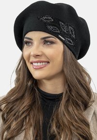 Berretto a maglia nero decorato con un motivo a foglia realizzato in perline, impreziosito da un dettaglio metallico sul lato. Il tessuto ha una consistenza morbida.