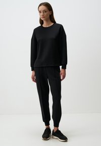 Felpa nera con colletto rotondo e spalle scese, abbinata a pantaloni jogger neri con polsini elastici e una texture liscia.