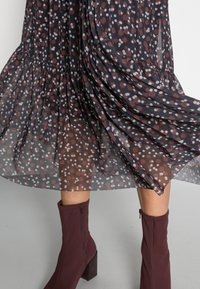 Černé a burgundské šaty s puntíkovaným vzorem v bílé a burgundské barvě, vyrobené z průhledného materiálu; mají vrstvený design a splývavou texturu.