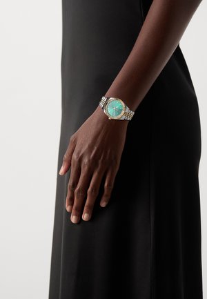 Montre-bracelet en or et argent avec un cadran turquoise, dotée d'index horaires métalliques, d'une lunette texturée et d'un bracelet à maillons à carreaux.