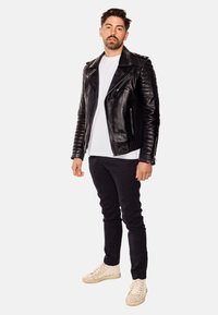 Svart läderbikerjacka med vadderade axeldetaljer, vit t-shirt under, mörka jeans och ljusa sneakers.