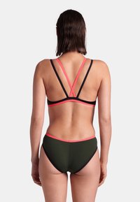 Bikini-Set mit einem schwarz-korallenfarbigen, gekreuzten Design. Der BH hat Kreuzträger auf dem Rücken; die Slips sind olivgrün mit korallenfarbenen Akzenten. Weicher, dehnbarer Stoff.