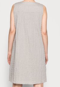 Sukienka bez rękawów w jasnoszarym teksturowanym materiale, z lekko marszczonym tyłem, długości powyżej kolan i luźnym kroju.