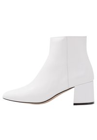 Bottine en cuir blanc avec un bout pointu et un talon épais. Texture lisse avec un design minimaliste et un subtil accent noir sur le talon.