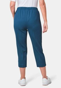 Teal cropped broek met een elastische tailleband, voorzien van een gladde textuur en op maat gemaakte naden, gecombineerd met witte sneakers.