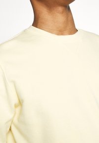 Felpa a girocollo in cotone di colore giallo chiaro, con colletto a costine e una vestibilità morbida, caratterizzata da una texture liscia e dettagli di cucitura minimi.