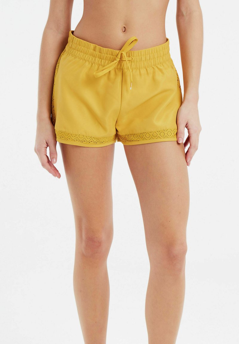 Gele shorts met elastische taille en een trekkoord, versierd met kant langs de onderrand. Zachte stof met een gladde textuur, geschikt voor casual kleding.