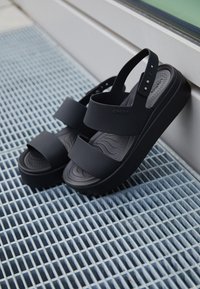 Black platform sandals made of rubber with two wide straps and an adjustable back strap. Textured footbed with a wavy pattern.