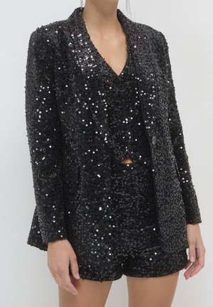Blazer noir à sequins et short à sequins assorti portés par une personne sur un fond clair uni.