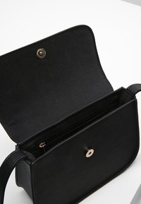 Černá kožená kabelka s klopou, vybavená zlatým patentním knoflíkem, vnitřní zipovou kapsou a hladkým, matným povrchem.