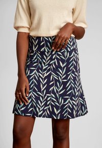 Laivastonsininen hame, jossa on mintunvihreitä ja kermankeltaisia lehtikuvioita. Valmistettu pehmeästä kankaasta, jossa on muotoiltu vyötärö ja helma levenee hieman.