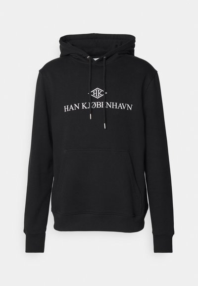 Črna kapuca z žepom spredaj, z belim besedilom "HAN KJØBENHAVN" in logotipom, izdelana iz mehke bombažne tkanine z rebrastimi manšetami.