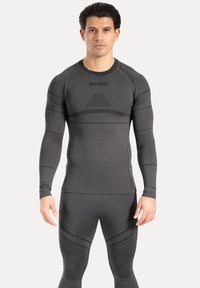 Langärmeliges Sportoberteil und enganliegende Hosen in Dunkelgrau, mit strukturierter Stoffoberfläche und kontrastierenden Streifenmustern sowie Logodetail.