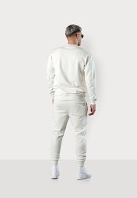Cream sweatshirt and matching joggers with elastic cuffs. Cotton blend material, minimal design, and small logo detail on the back.