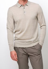 Suéter polo de manga larga en beige claro, confeccionado con una tela suave, que presenta un cuello con solapa, una tapeta con tres botones y puños acanalados.