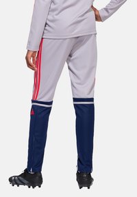 Graue Sporthose mit roten Streifen an den Seiten, marineblauen Unterteilen und Reißverschlussbündchen. Getragen mit schwarzen Fußballschuhen.