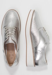 Chaussures argentées à lacets avec une tige en cuir texturé et des accents lisses, une semelle blanche et des détails marron clair.