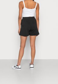 Svarta shorts i mjukt material med elastisk midja, kombinerat med en vit crop top. Outfiten fulländas med vita sneakers.