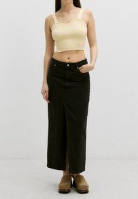 Zwarte denim maxi-jurk met een split aan de voorkant, gecombineerd met een lichtgele geribde cropped top met brede banden. Casual schoeisel maakt de look compleet.