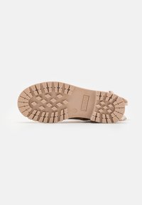 Lys beige gummistøvelsåle med et teksturert mønster og merkevare. Har en rund form og solid konstruksjon for godt grep.