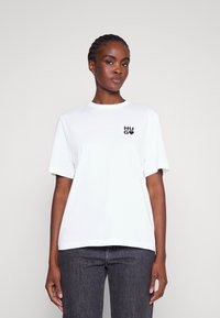 Valge puuvillane t-särk lühikeste varrukatega, mille vasakul rinnal on must "HUG" logo. Esteetiline lõikega ja ümar kaelus.