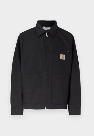 Veste noire zippée avec col, deux poches avant, et petite écusson logo sur la poche poitrine gauche.