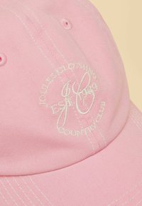 Gorra de béisbol rosa claro con texto bordado en blanco "Joules Clothing Country Club Est. 1989" en el panel frontal.