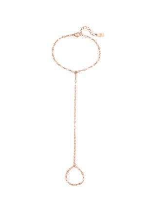 Cadena de mano de oro rosa con cuentas enlazadas, que conecta la pulsera en la muñeca con un anillo en el dedo, llevada sobre una manga de color claro.