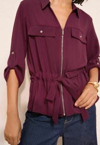 Burgundi värvi pluus kerge materjali, esiTasku kahe rinnaTaskuga ja voltimisega vööga, mis on seotud vastava vööga.