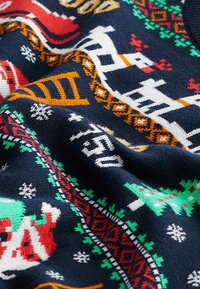 Tissu tricoté festif avec des rennes blancs, des sapins de Noël verts, des flocons de neige rouges et blancs, et des motifs géométriques sur un fond bleu foncé.