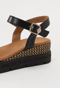 Sandale en cuir noir avec une large sangle, boucle réglable et une semelle plateforme texturée en beige et marron.