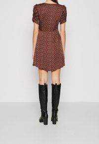 Robe rouge à fleurs avec manches bouffantes, taille cintrée et jupe évasée. Associée à des bottes hautes noires en cuir avec talons carrés.