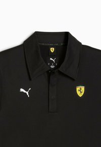 Cămașă polo neagră cu guler plat, având un logo alb Puma și un emblema a scutului Ferrari galben cu un detaliu de cal pe piept.