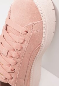 Gros plan sur une sneaker en daim rose avec de larges lacets en nylon et une épaisse semelle en caoutchouc blanc texturé.