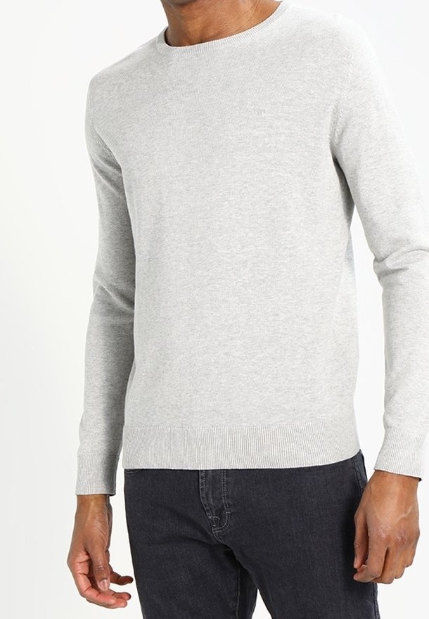 Hellgrauer Pullover mit Rundhalsausschnitt, gerippten Bündchen und Saum. Aus weichem Material, taillierte Passform, getragen über dunklen Jeans.