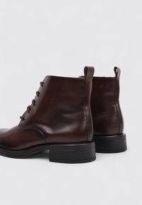 Brown leather ankle boots with a smooth texture, round toe, and five eyelets for laces. Sturdy black rubber sole; pull tab at the back.