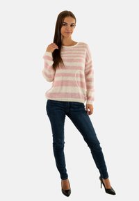 Pull à rayures rose clair et blanc, avec une coupe loose et un ourlet côtelé, associé à un jean skinny bleu foncé et des chaussures à talons hauts noires.