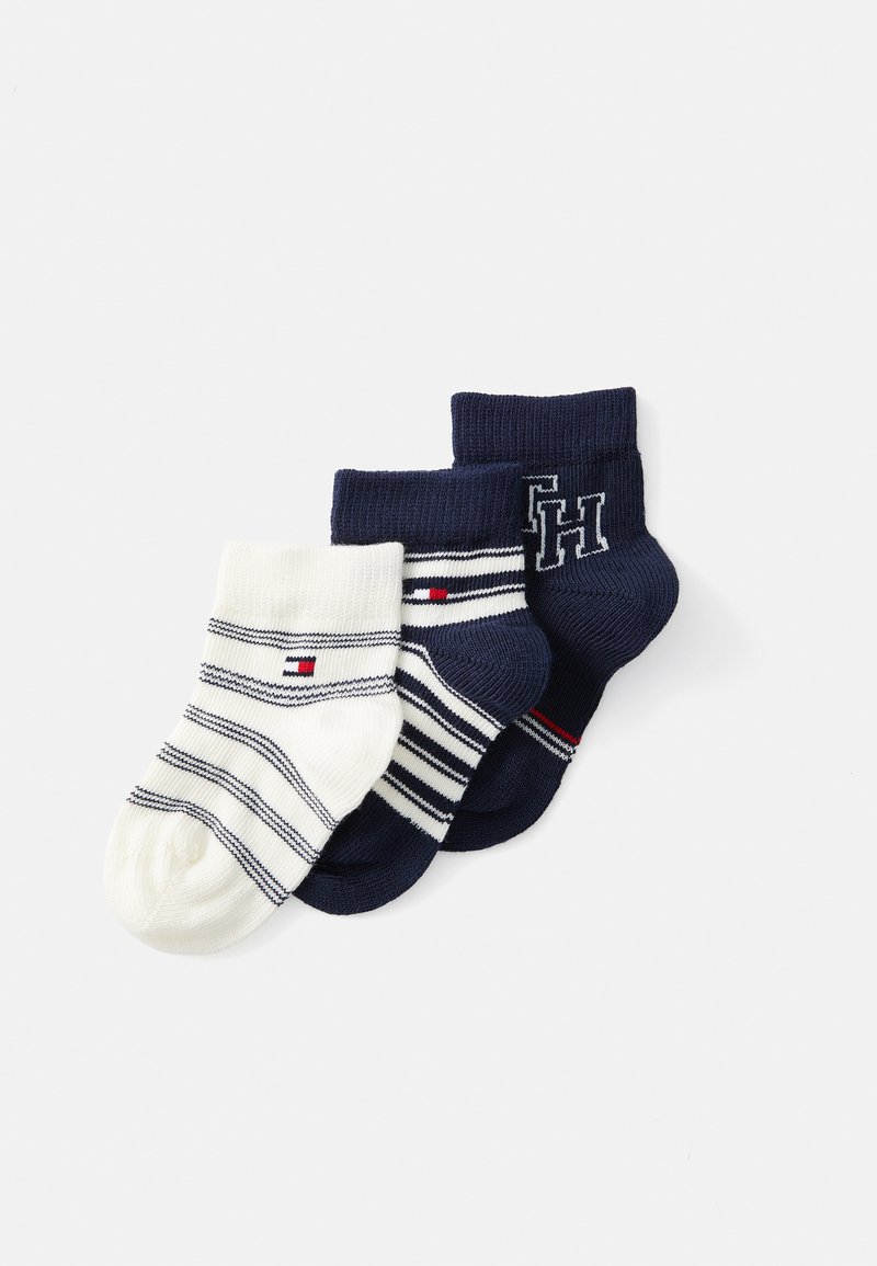 Tres pares de calcetines: uno crema con rayas marino, uno marino con rayas blancas y uno azul marino sólido con un logo. Mezcla de algodón, textura acanalada.
