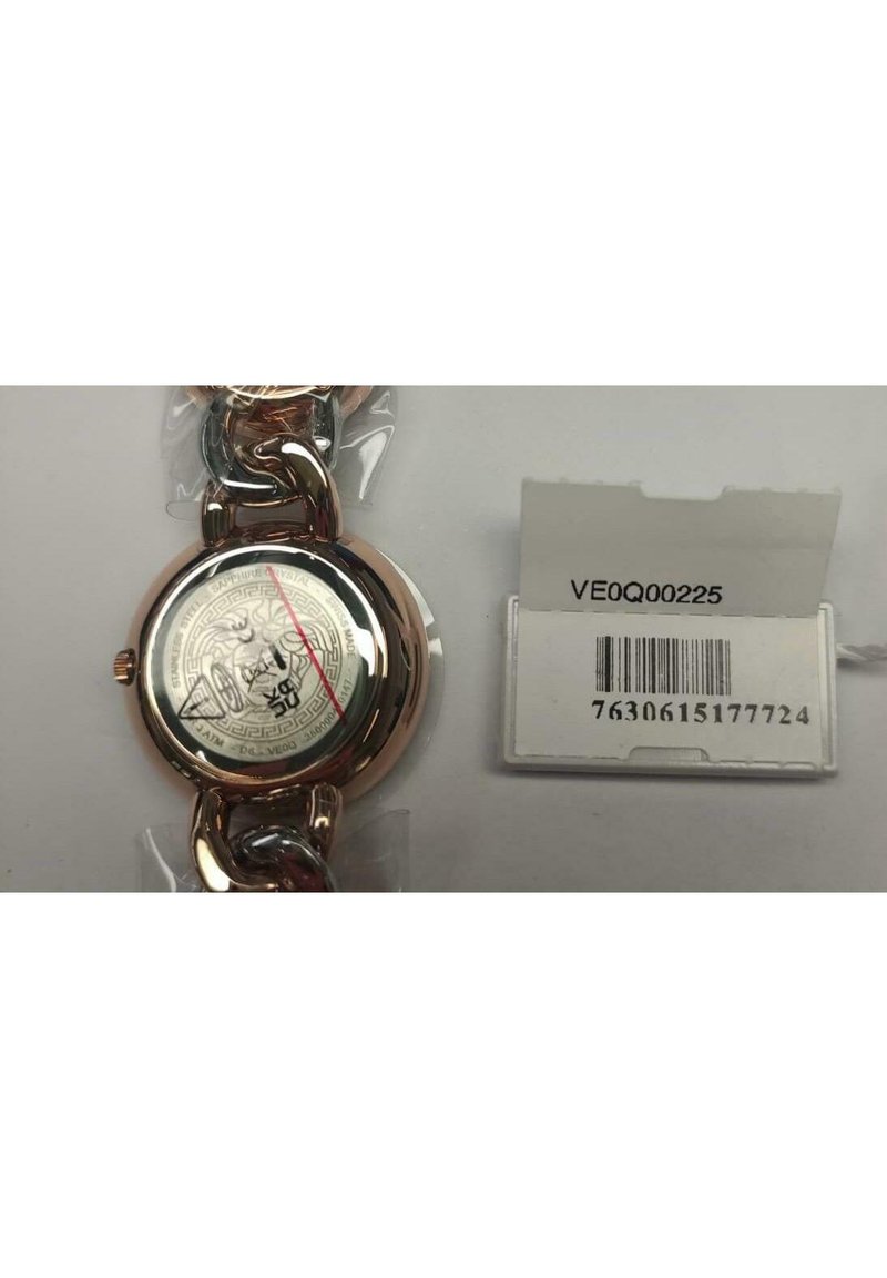 Round watch with a stainless steel and rose gold chain. The back displays a decorative pattern and inscription. Includes a price tag.