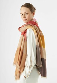 Écharpe douce en tissu avec des rayures horizontales dans des tons chauds : rouge, orange, beige et marron. Fini avec des bords frangés pour ajouter de la texture.