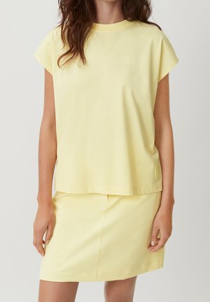 Gelbes Baumwoll-T-Shirt mit kurzen Ärmeln, legerer Passform und rundem Ausschnitt, kombiniert mit einem passenden Rock. Keine sichtbaren Muster oder Akzente.